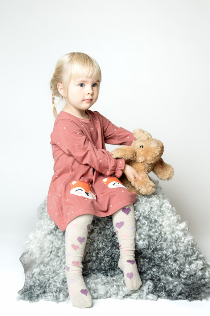 Porträtt i studio av blond flicka i rosa klänning med nallebjörn