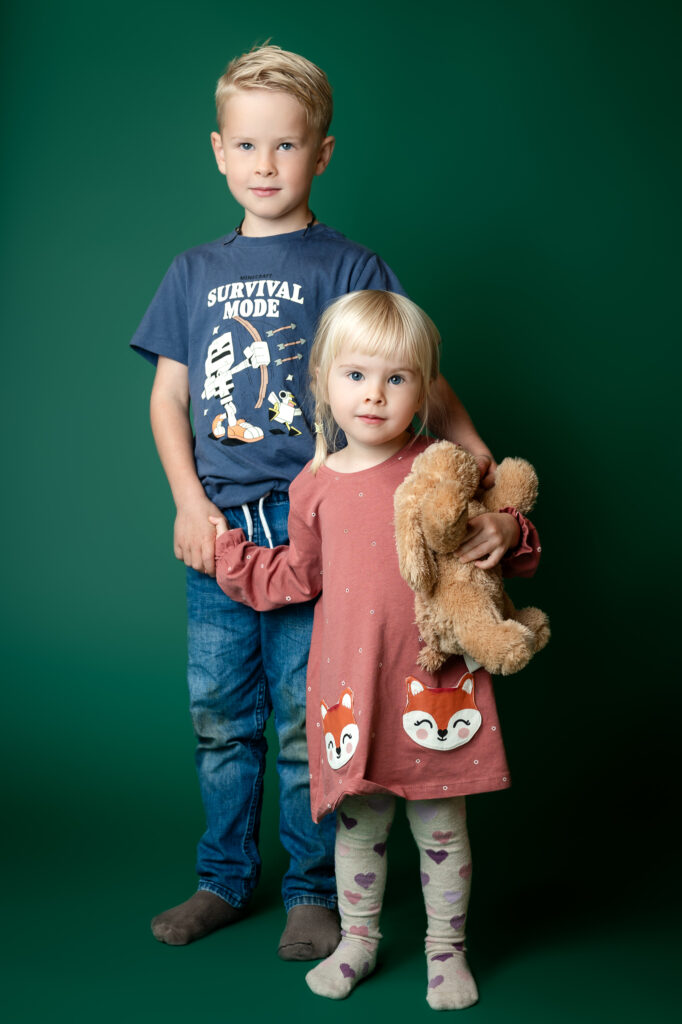 Porträttbild av två syskon, en pojke och en flicka mot en grön bakgrund i studio